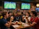 Cheering fans analyzing kèo bóng đá odds in a lively sports bar during a football match.