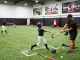 Youth baseball training at Hitclub with coach demonstrating techniques and players practicing in a well-lit indoor facility.